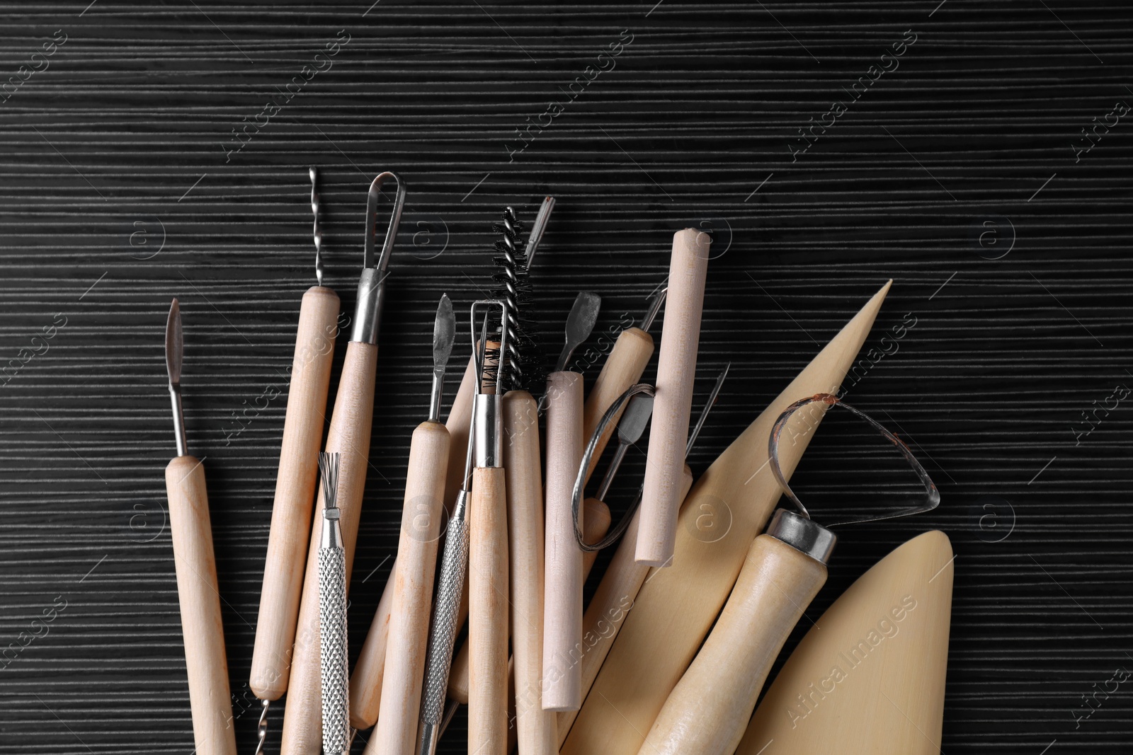 Photo of Clay and set of modeling tools on dark gray wooden table, flat lay
