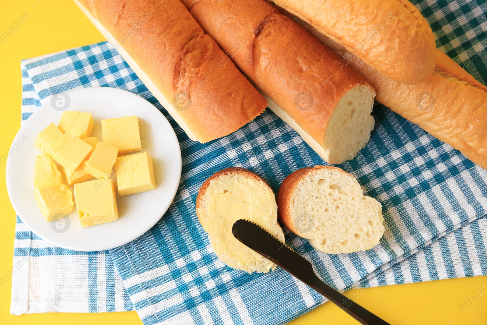 Photo of Whole and cut baguettes with fresh butter on yellow background, top view