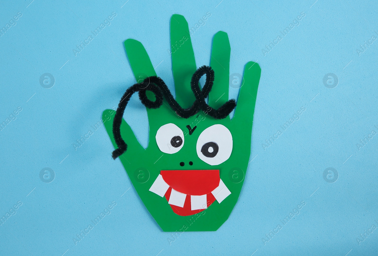 Photo of Funny green hand shaped monster on light blue background, top view. Halloween decoration