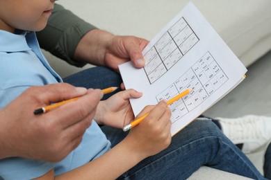 Photo of Little boy with his grandfather solving sudoku puzzle on sofa at home, closeup
