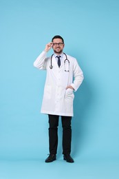 Full length portrait of smiling doctor on light blue background