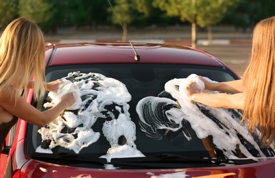 Photo of Young women washing car with sponges outdoors