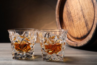 Photo of Glasses with whiskey and wooden barrel on table