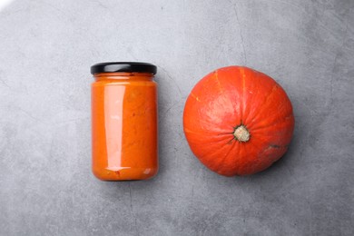 Photo of Jar of pumpkin jam and fresh pumpkin on grey table, flat lay