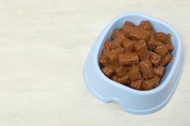 Photo of Wet pet food in feeding bowl on white table, space for text