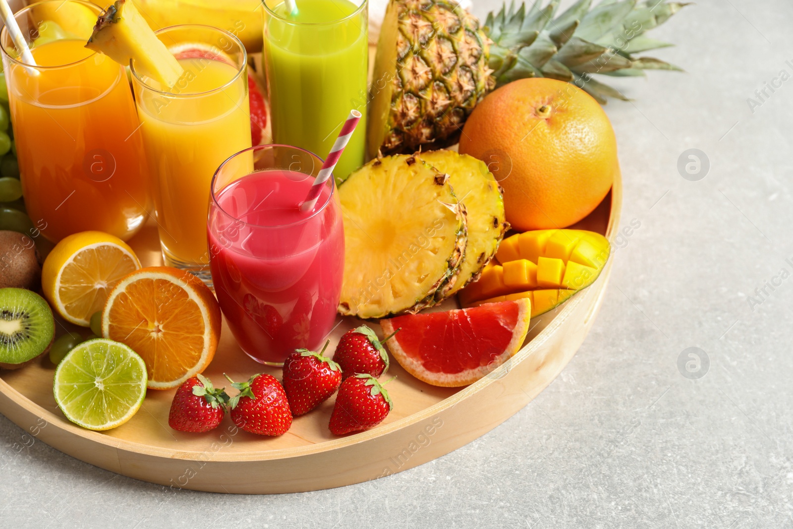 Photo of Wooden tray with glasses of different juices and fresh fruits on table