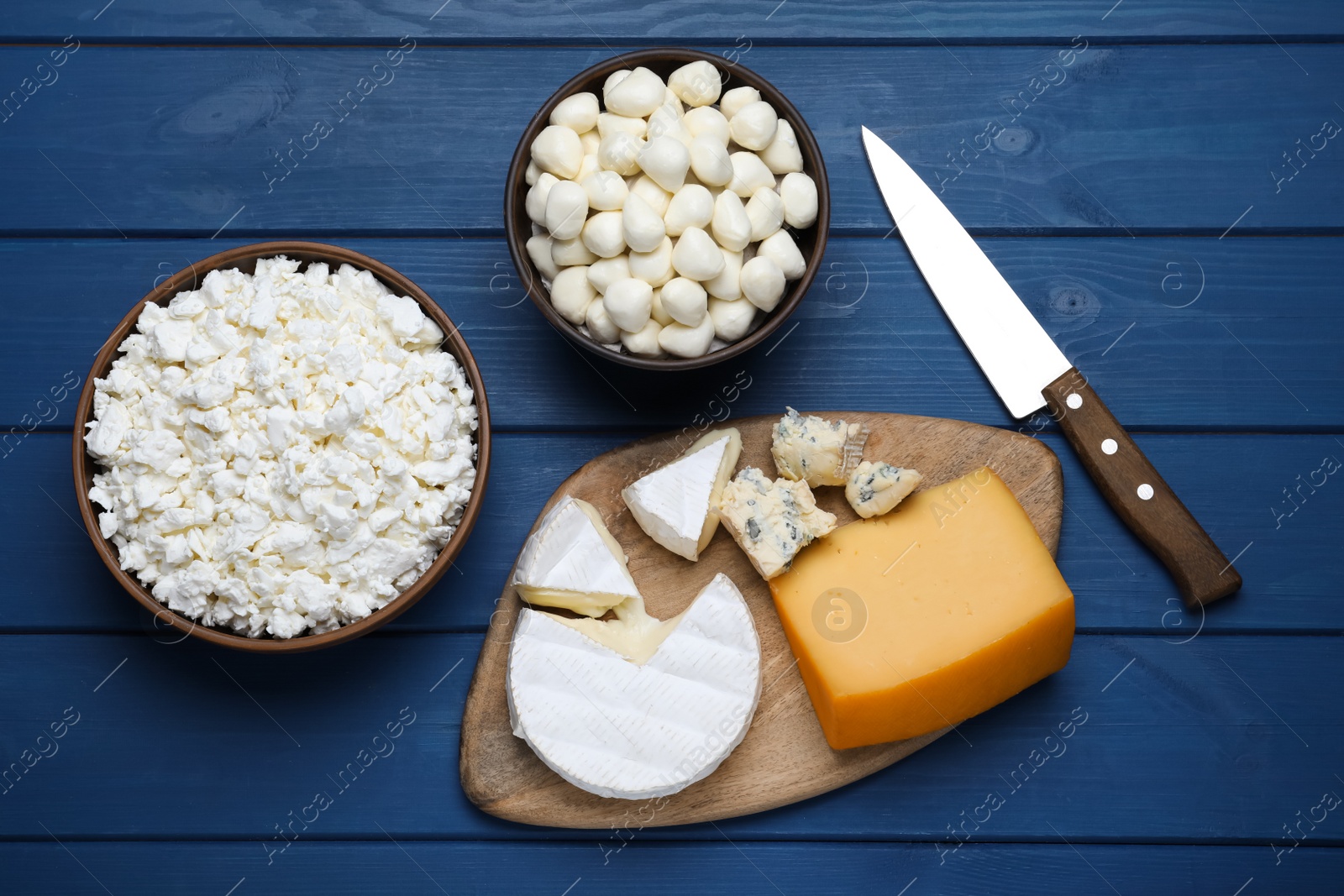 Photo of Clay dishware with fresh dairy products on blue wooden table, flat lay