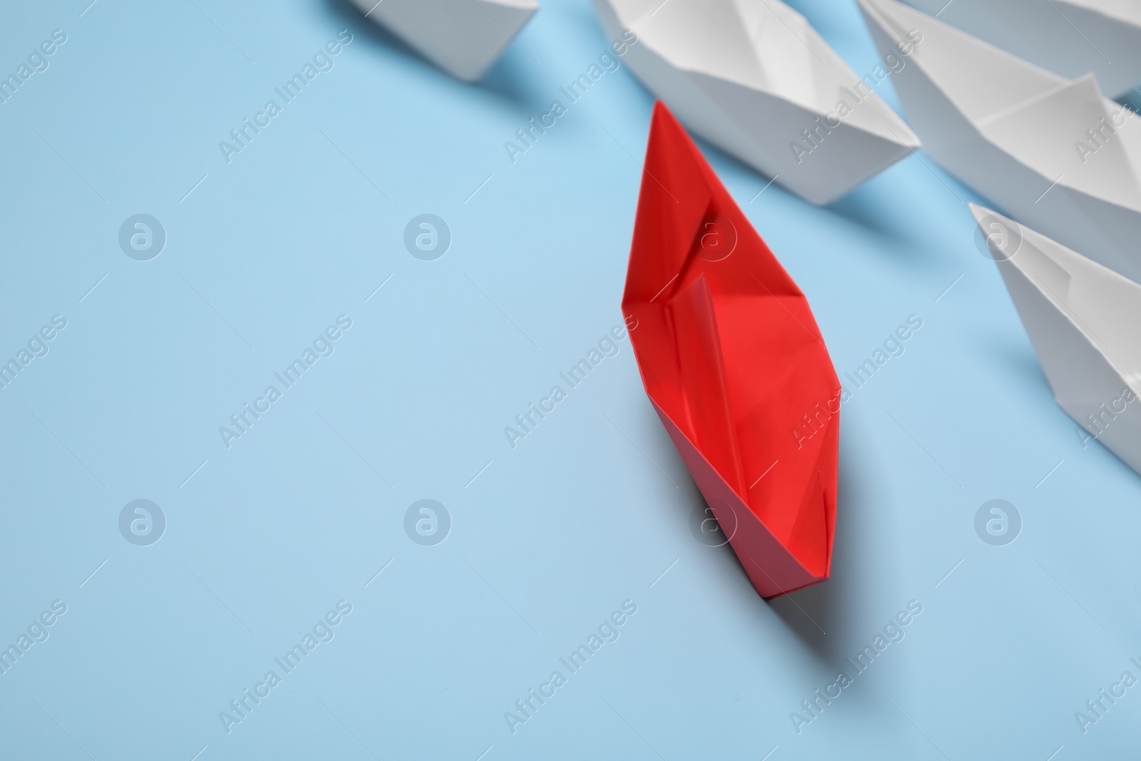 Photo of Red paper boat among others on light blue background, space for text. Uniqueness concept