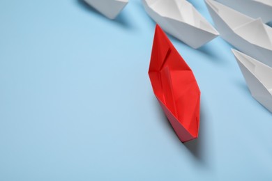 Photo of Red paper boat among others on light blue background, space for text. Uniqueness concept
