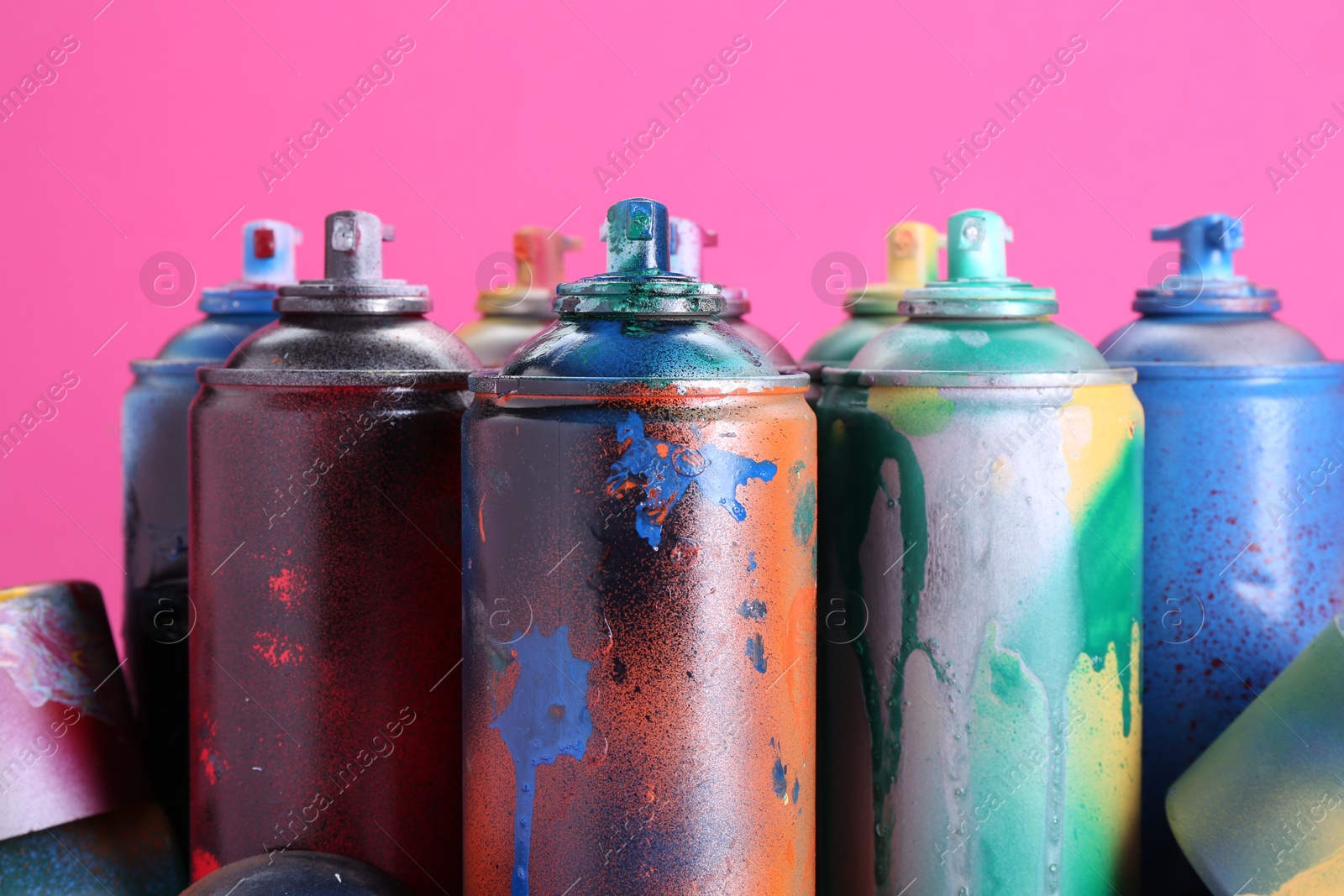 Photo of Many spray paint cans on pink background, closeup