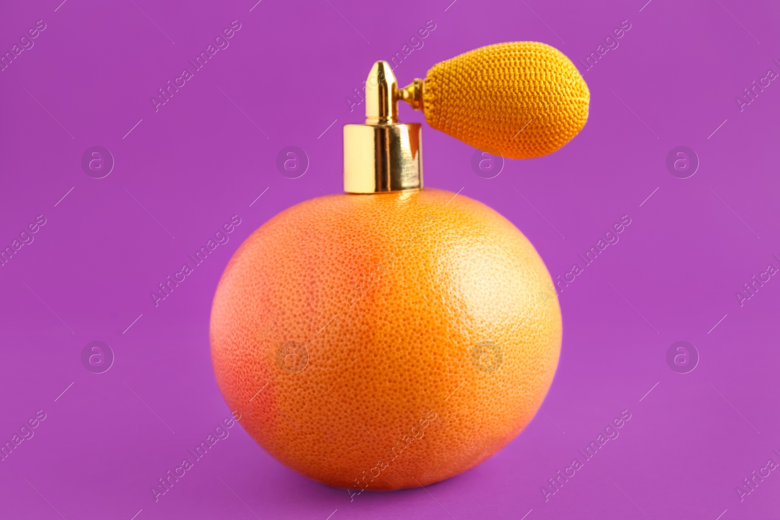 Photo of Grapefruit with vintage atomizer imitating perfume on violet background