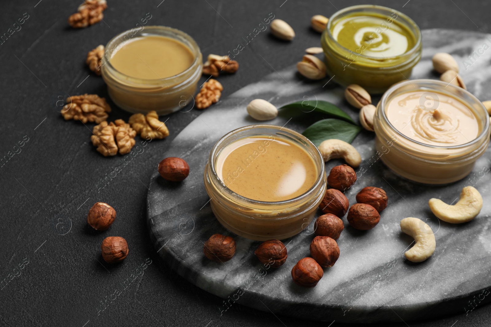 Photo of Jars with butters made of different nuts and ingredients on black table