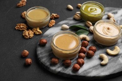 Jars with butters made of different nuts and ingredients on black table