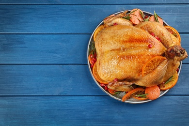 Photo of Roasted chicken with oranges on blue wooden table, top view. Space for text