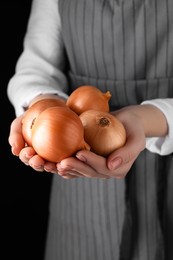Woman holding ripe onions on black background, closeup