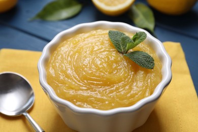 Photo of Delicious lemon curd in bowl and spoon on table, closeup
