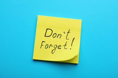 Photo of Paper note with phrase Don' t Forget on blue background, top view