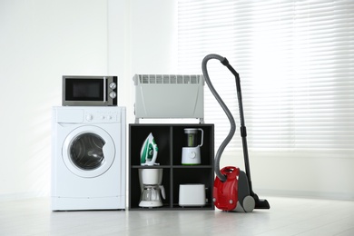 Photo of Modern vacuum cleaner and different household appliances near window indoors