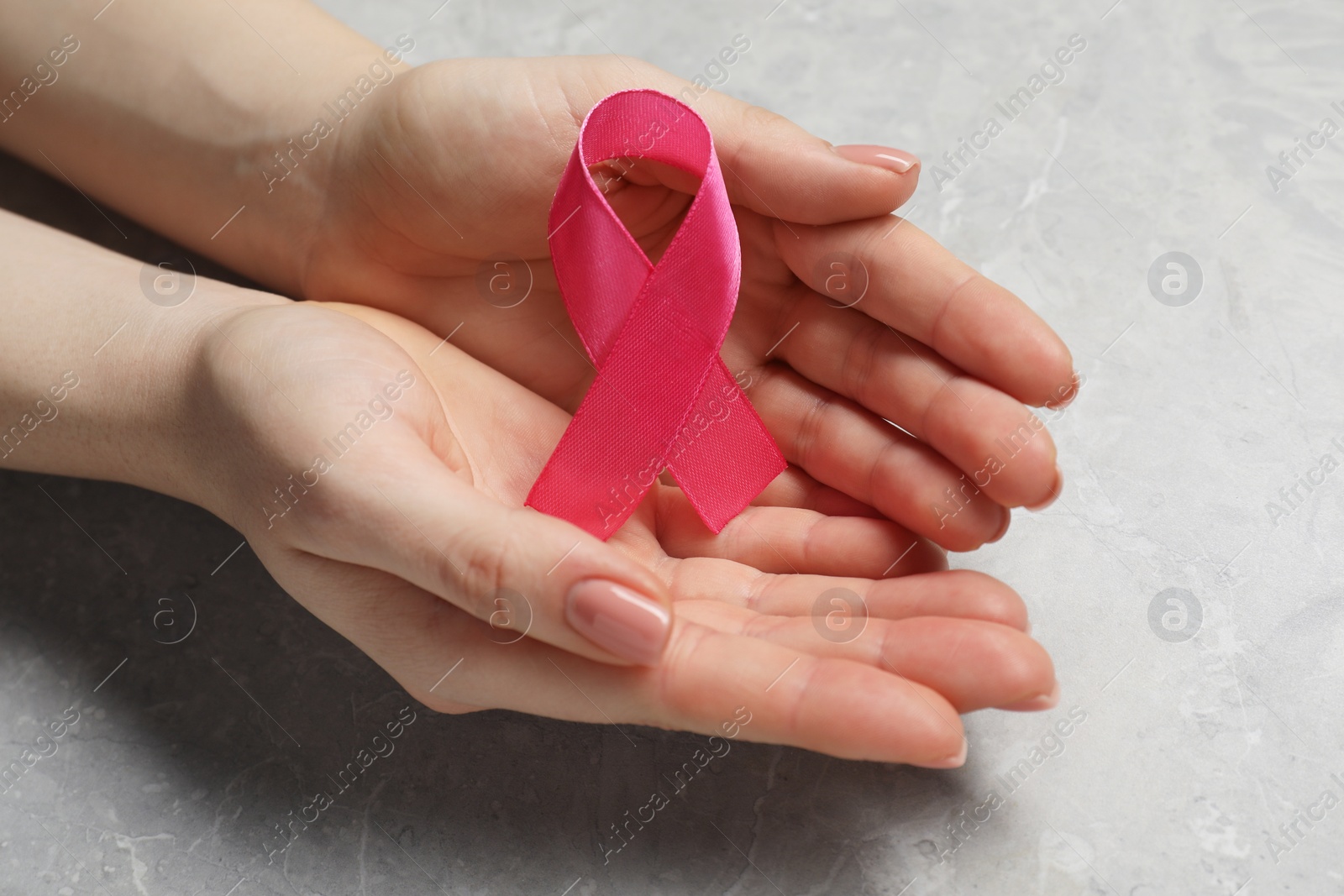 Photo of Woman with pink ribbon at grey marble table, closeup. Breast cancer awareness