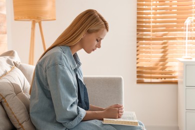 Religious young woman with Bible praying indoors. Space for text