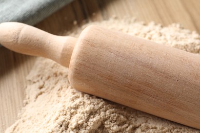 Photo of Pile of flour and rolling pin on wooden table, closeup