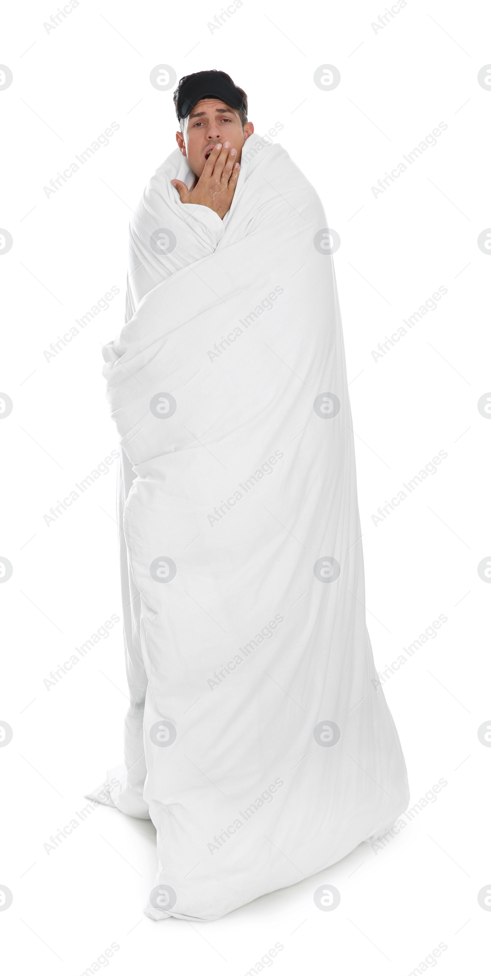 Photo of Man in sleeping mask wrapped with blanket yawning on white background