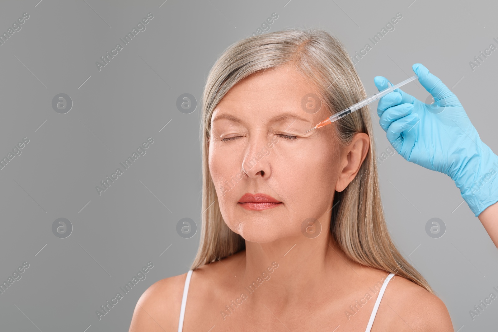 Photo of Doctor giving facial injection to senior woman on light grey background, closeup and space for text. Cosmetic surgery