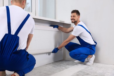 Professional plumbers installing new heating radiator in room
