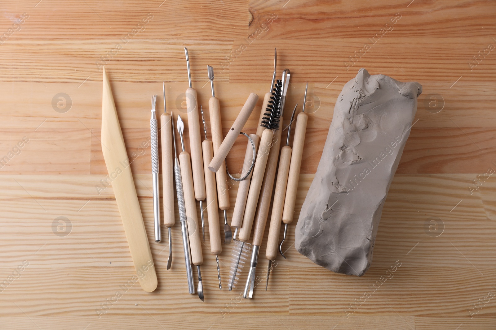 Photo of Clay and set of modeling tools on wooden table, flat lay