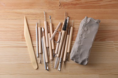 Clay and set of modeling tools on wooden table, flat lay