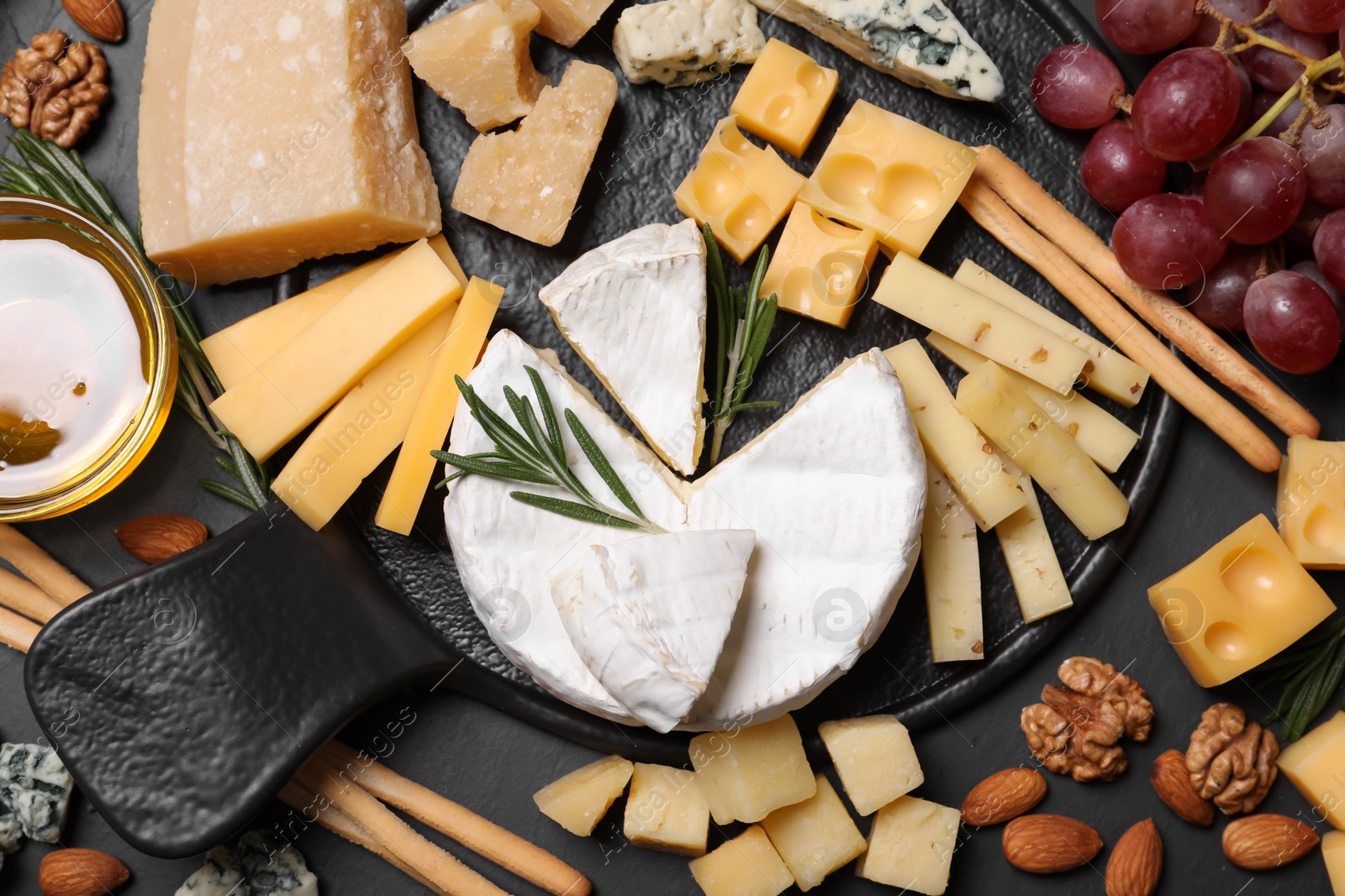 Photo of Cheese plate with honey, grapes and nuts on black table, flat lay