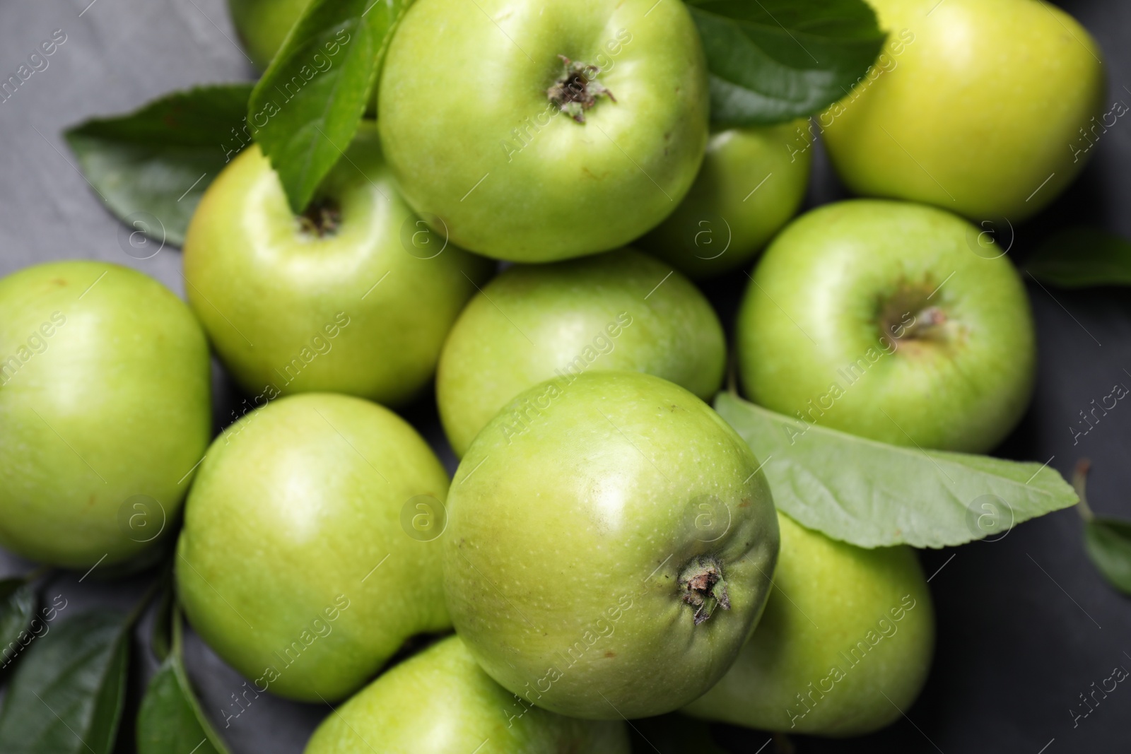 Photo of Ripe green apples with leaves on dark grey table, closeup