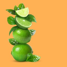 Image of Stacked cut and whole limes with green leaves on orange background, space for text