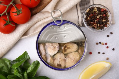 Photo of Open tin can with mackerel chunks, spices and tomatoes on grey table, flat lay