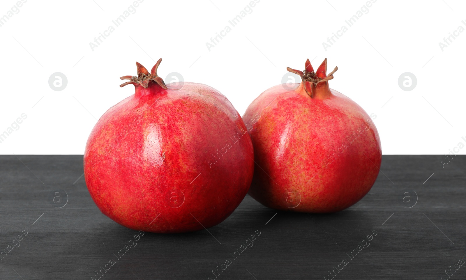 Photo of Fresh pomegranates on black wooden table against white background