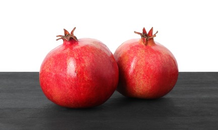 Fresh pomegranates on black wooden table against white background