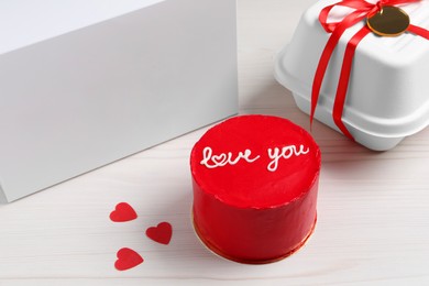 Photo of Bento cake with text Love You and takeaway packaging on white wooden table