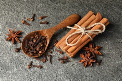 Wooden spoon with different spices on gray textured table, flat lay