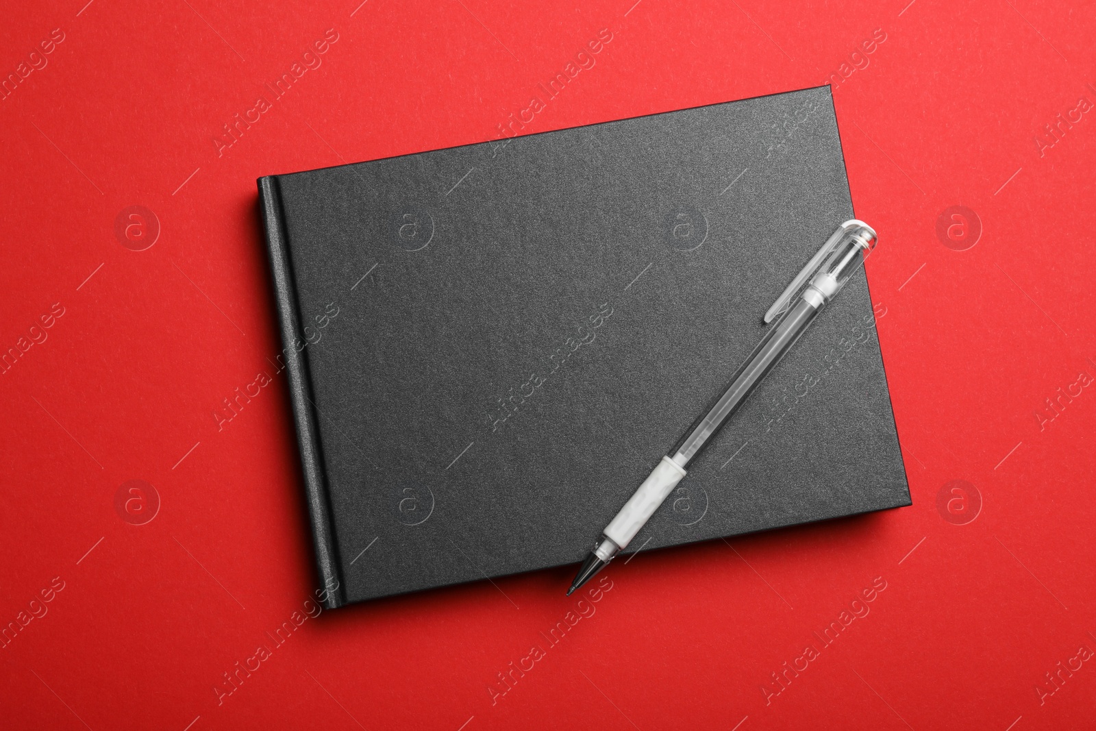 Photo of Stylish black notebook and pen on red background, top view