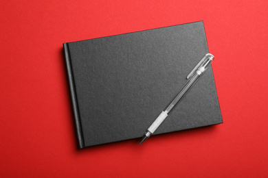 Stylish black notebook and pen on red background, top view