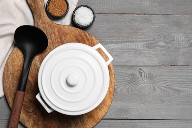 White pot, board, ladle and spices on grey wooden table, flat lay. Space for text