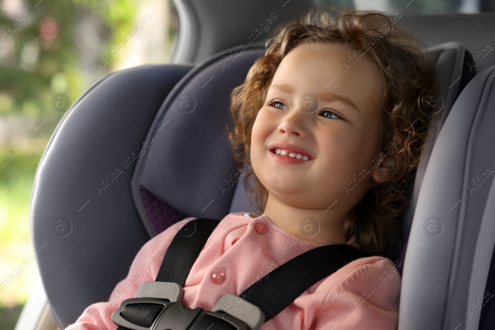 Photo of Cute little girl sitting in child safety seat inside car