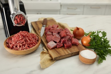 Electric meat grinder with beef and products on white marble table indoors