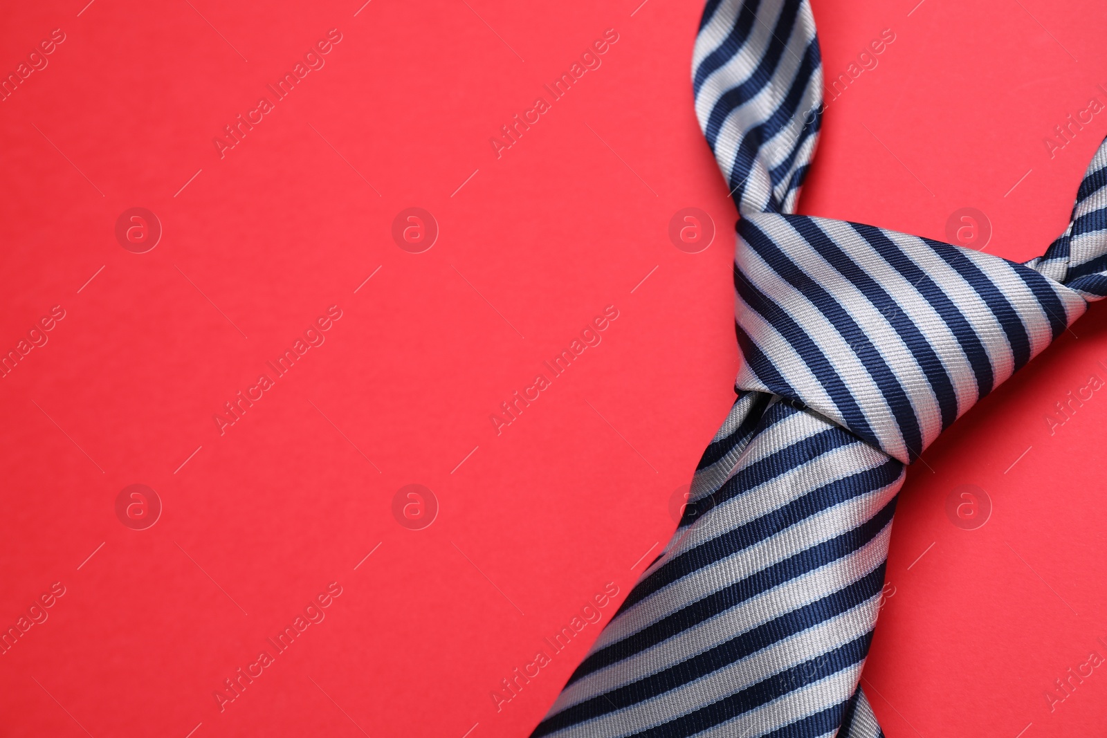 Photo of Striped necktie on red background, closeup. Space for text