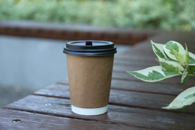 Photo of Paper cup on wooden bench outdoors. Takeaway drink
