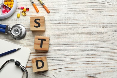 Flat lay composition with abbreviation STD and stethoscope on white wooden table. Space for text