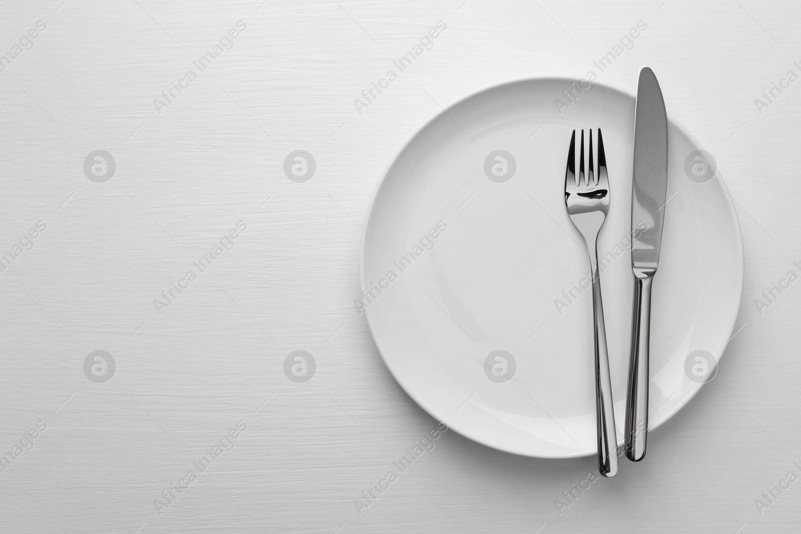Photo of Clean plate, fork and knife on white table, top view. Space for text
