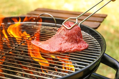 Photo of Tasty meat on barbecue grill with fire flames outdoors, closeup