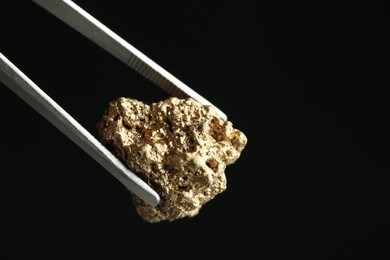 Photo of Tweezers with gold nugget against black background, closeup. Space for text