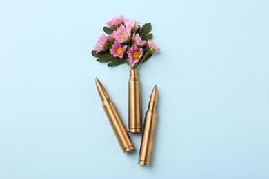 Photo of Bullets and cartridge case with beautiful flowers on light blue background, flat lay